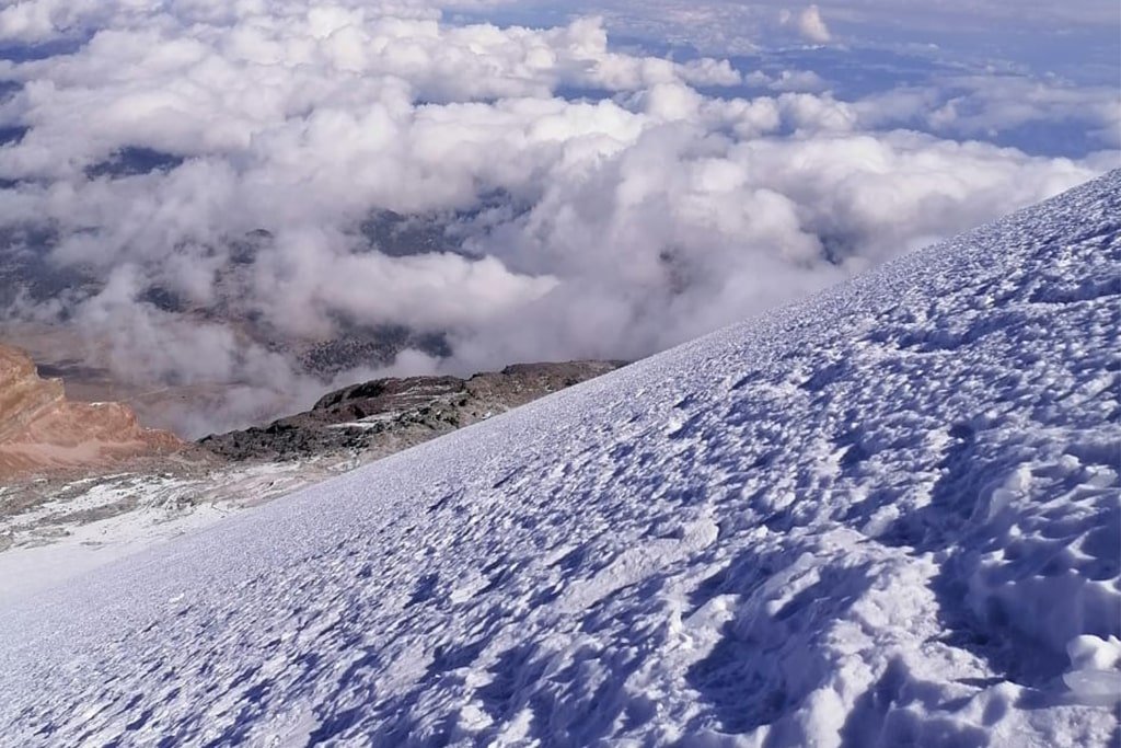 A climber in a red jacket looking over a sea of clouds